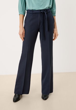 Marineblauwe op maat gemaakte broek met een wide-leg ontwerp, een riem in de taille en een gladde stoftextuur. Gecombineerd met een lichtgroene top en zwarte enkellaarsjes.