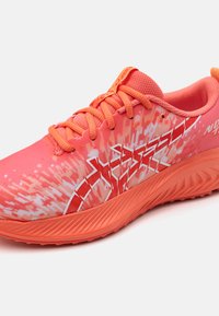 Baskets d'entraînement rose vif avec une tige en mesh texturé, accents rouges, motif en zigzag et semelle en caoutchouc striée pour l'adhérence.