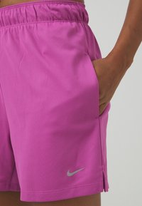 Pantaloncini sportivi viola con vita elasticizzata, tasche laterali e logo riflettente argento nella parte anteriore inferiore sinistra. Tessuto dall'aspetto liscio.