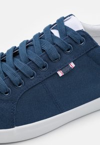 Sneakers in tela di colore blu navy con lacci coordinati, suola in gomma bianca e linguetta con strisce rosse e blu.