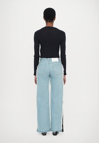 Top negro de manga larga con textura acanalada, combinado con vaqueros de pierna ancha de color azul claro, con bordes deshilachados y una etiqueta blanca en el bolsillo trasero.