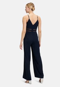 Combinaison sans manches bleu marine avec un corsage ajusté et des pantalons à jambe large, présentant des accents en maille à la taille et un dos en V.