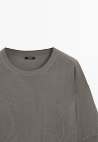T-shirt gris à manches courtes avec col rond, en tissu tricoté, avec une étiquette de marque visible à l'intérieur du col.