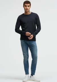 Navyblaues Langarm-T-Shirt mit Rundhalsausschnitt aus einem weichen Stoff, kombiniert mit hellblauen Slim-Fit-Jeans und weißen Sneakers. Saubere Nähte.