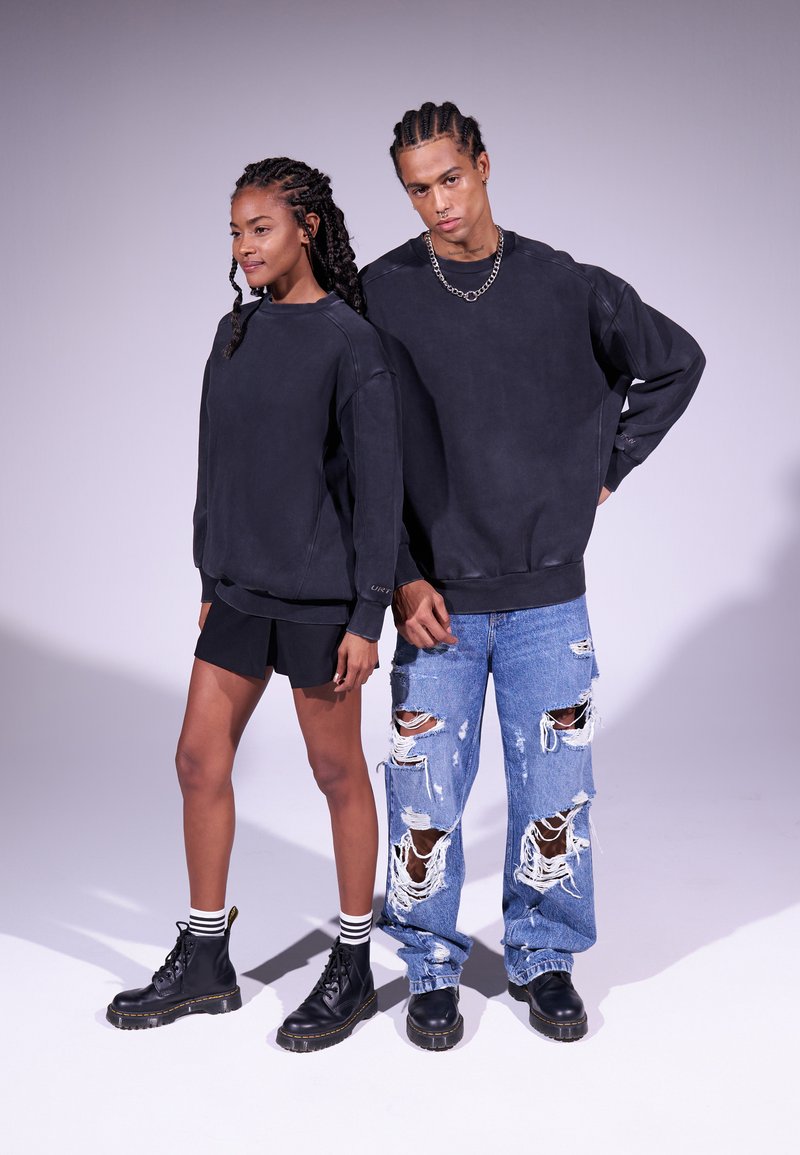 Sudaderas negras de gran tamaño combinadas con jeans claros rasgados y botas negras. La mujer lleva pantalones cortos negros y calcetines a rayas.