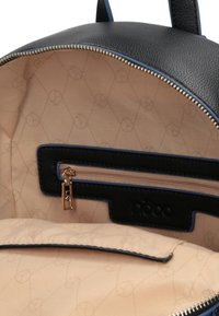 Interiér černé kožené tašky s béžovou textilní podšívkou, zipovou kapsou a vyraženým logem na černém koženém štítku.