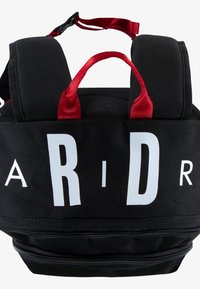 Mochila negra con acentos rojos, correas acolchadas y un asa en la parte superior. Presenta un texto en blanco audaz "ARID" en la parte frontal y un compartimento con cremallera en la parte inferior.