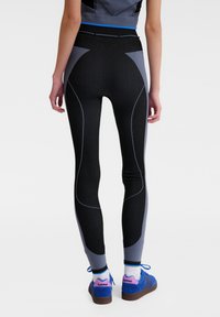 Zwarte en grijze sportleggings met ribbeltextuur, gecontourde panelen en een hoge taille. Bevat contrasterende blauwe stiksels en accenten.
