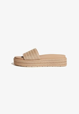Beige platform slidesandaal met brede band van geweven textuur en bijpassende dikke, gestructureerde zool op een witte achtergrond.