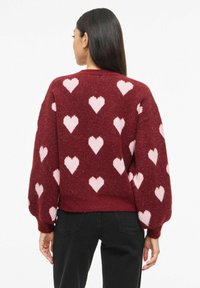 Bordo džemper s uzorcima ružičastih srca, opuštenog kroja i balon rukava. Teksturirano pletenje s rebrastim rubom i manžetama.