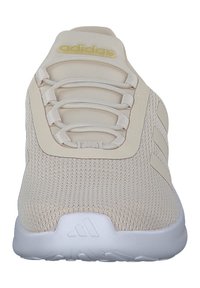 Baskets Adidas beiges avec tige en tricot, lacets élastiques, logo doré sur la languette, trois bandes sur le côté et semelle blanche avec logo en relief.