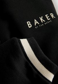 Sort sweater med hvid "BAKER BY TED BAKER" logo. Har ribbet halsudskæring og manchetter med fine hvide striber. Blød stofstruktur.