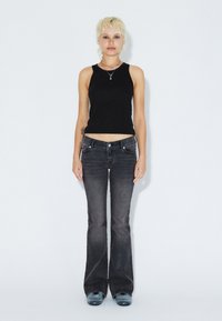 Black sleeveless top paired with dark grey flared jeans. The outfit features a mid-rise waist and a classic five-pocket design.