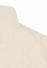 Gesteppter cremefarbener Jackenkragen mit einer gerippten Strickstruktur und einem gesteppten Muster, mit seitlichem Taschen-Detail. Weiches Stoffaussehen.