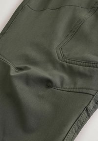 Suurplaan oliivrohelisest kangast, millel on topeltõmblused ja rõivast seljatasku detail.