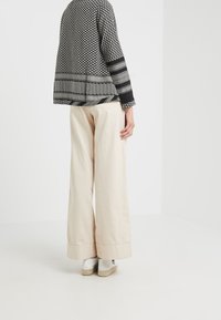 Maglione oversize a righe bianche e nere con maniche lunghe, abbinato a pantaloni larghi di colore beige chiaro e scarpe espadrillas bianche.
