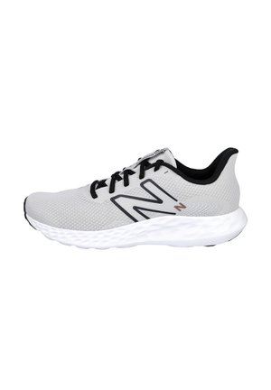 Zapatilla atlética gris con una parte superior de malla transpirable, cordones negros y suela blanca en contraste. Presenta un logo negro prominente en el lateral.