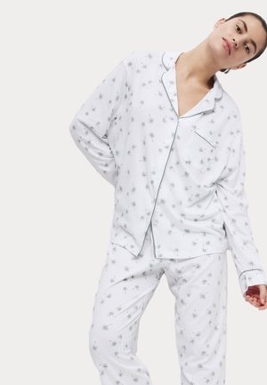 Vitt pyjamaset med ett mönster av små gröna stjärnliknande former. Skjortan har krage, bröstficka och kontrasterande kant.