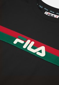 Musta t-paita, jossa on paksu punavihreä raidallinen nauha ja suuri valkoinen "FILA"-logo sileällä pinnalla.