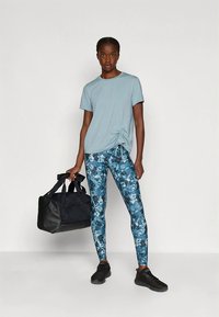 Light blue short-sleeve t-shirt with gathered side, floral-patterned blue leggings, black shoes, and a black duffel bag.