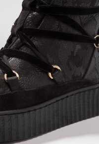 Mustat kengät, joissa on yhdistelmä teksturoitua nahkaa ja mokkaa, kultaiset yksityiskohdat ja paksu uritettu musta pohja.