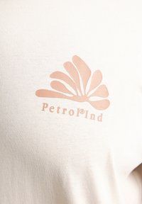 Crèmekleurig katoenen t-shirt met een beige abstract ontwerp en de tekst "Petrol®Ind" onder de afbeelding gedrukt. Zachte textuur, casual fit.