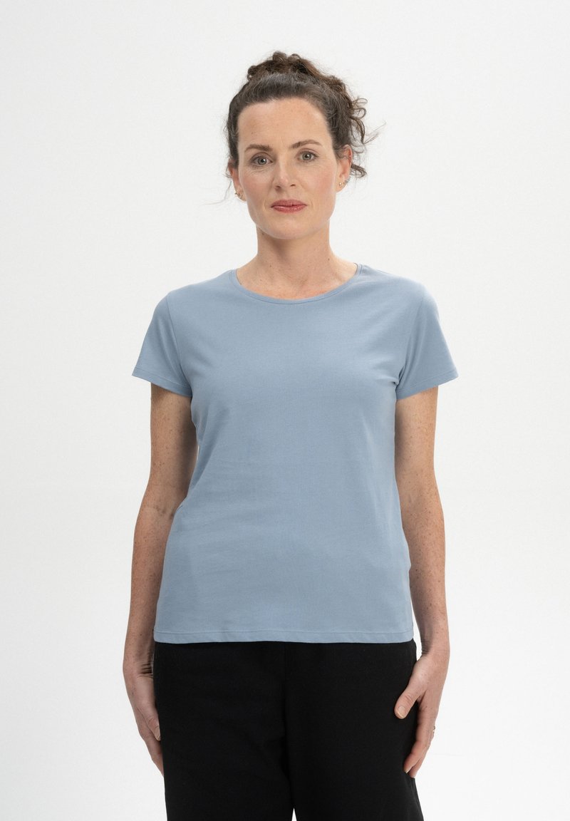 Hellblaues T-Shirt mit kurzen Ärmeln aus glattem Stoff, mit Rundhalsausschnitt und lockerer Passform, kombiniert mit schwarzen Hosen.