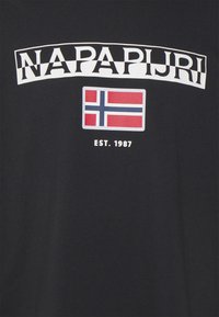 Sort t-shirt med "NAPAPIJRI" i fed hvid tekst over et grafisk billede af det norske flag; "EST. 1987" trykt nedenunder. Glat, bomulds materiale.
