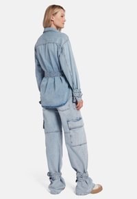 Lichtblauwe denim overhemd met een riem in de taille en knoopmanchetten, gecombineerd met lichtblauwe cargobroek met meerdere zakken en geknoopte zoom.