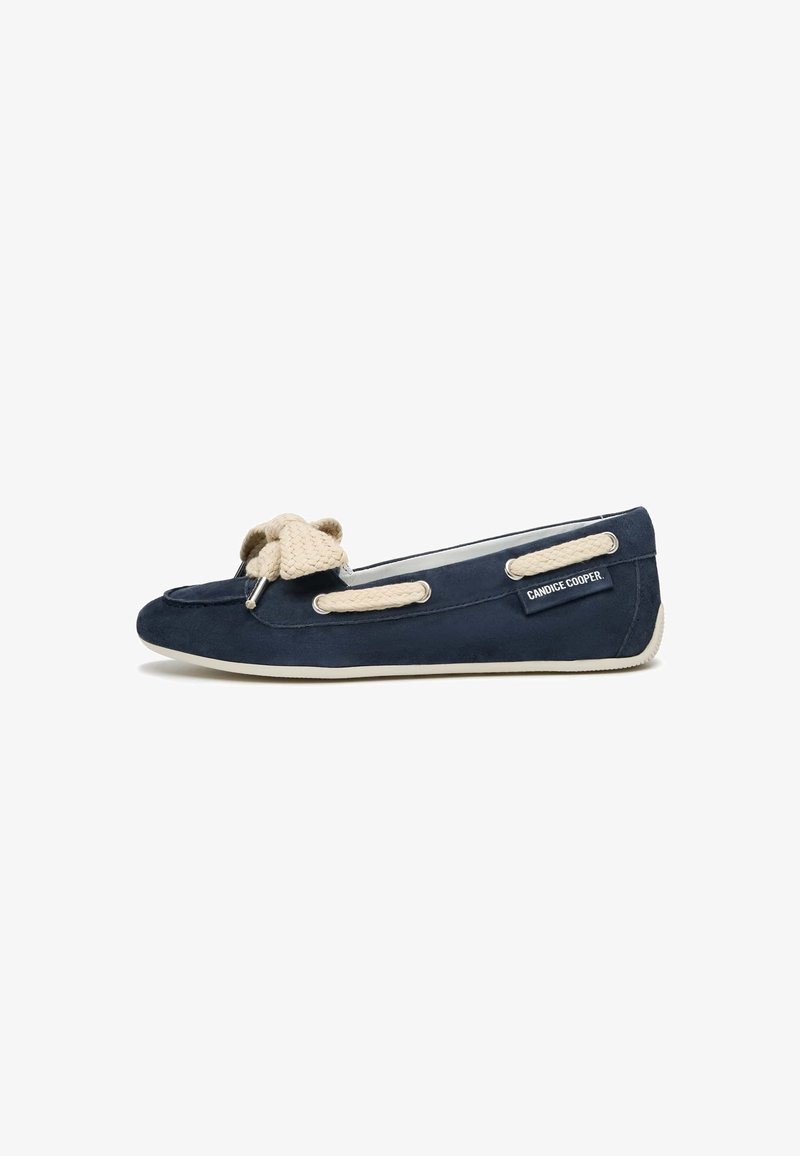 Scarpa piatta in suede blu navy con un fiocco beige testurizzato, suola bianca e branding laterale. Presenta dettagli in pizzo sulla parte superiore.