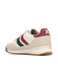 Zapatilla beige con materiales de ante y cuero, que presenta franjas rojas y verdes, un collar acolchado y suela blanca con plantilla de goma.