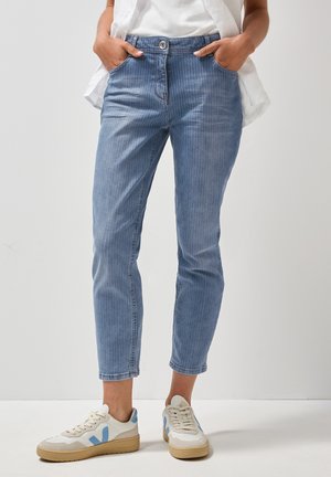 Jean en denim rayé bleu clair avec une coupe slim, comprenant des poches avant, une fermeture à bouton, et des baskets assorties avec des accents bleus.