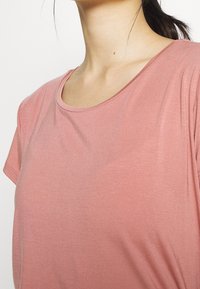 T-shirt a maniche corte di colore rosa chiaro, con scollatura rotonda e texture morbida e liscia, che enfatizza la semplicità nel design.