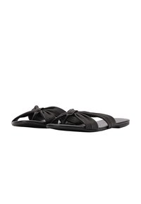 Sandali neri flat realizzati in pelle testurizzata, con cinturini annodati e un design minimalista con una suola liscia e imbottita.