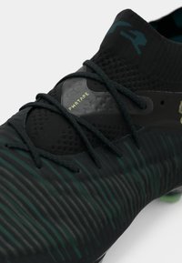 Black and green football boot with a textured upper, featuring narrow stripes and a smooth toe cap. Includes lacing and logo detail.