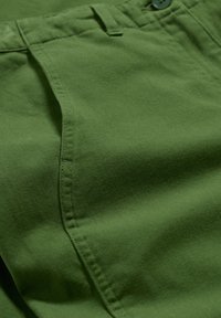 Grön bomullstyg med en slät tekstur, som har en sydd sid söm och en knappdetalj vid midjan.