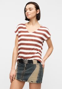 Γυναίκα που φορά κορυφή με ριγέ καφέ και λευκά κοντά μανίκια, μπαίνει μέσα σε μίνι φούστα από τζιν δύο αποχρώσεων με πόρπη ζώνης σε σχήμα καρδιάς.