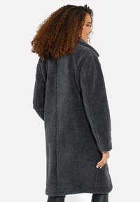 Grau teddy Mantel mit plüschiger Textur, langen Ärmeln und Kragen. Hat einen geraden Schnitt und reicht bis zur Mitte des Oberschenkels. Nahtdetails auf der Rückseite.