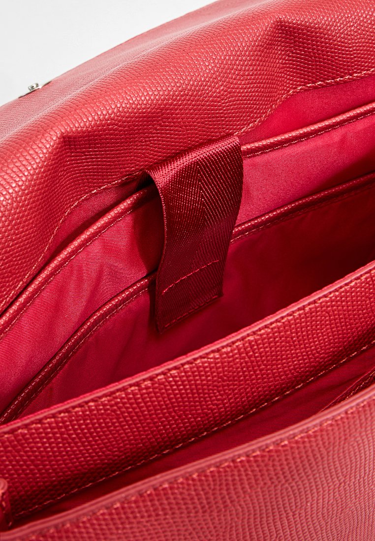 Roter strukturierter Handtascheninnenraum mit glatter Fütterung, unterteilten Fächern und einem genähten Akzentriemen für einfachen Zugriff.