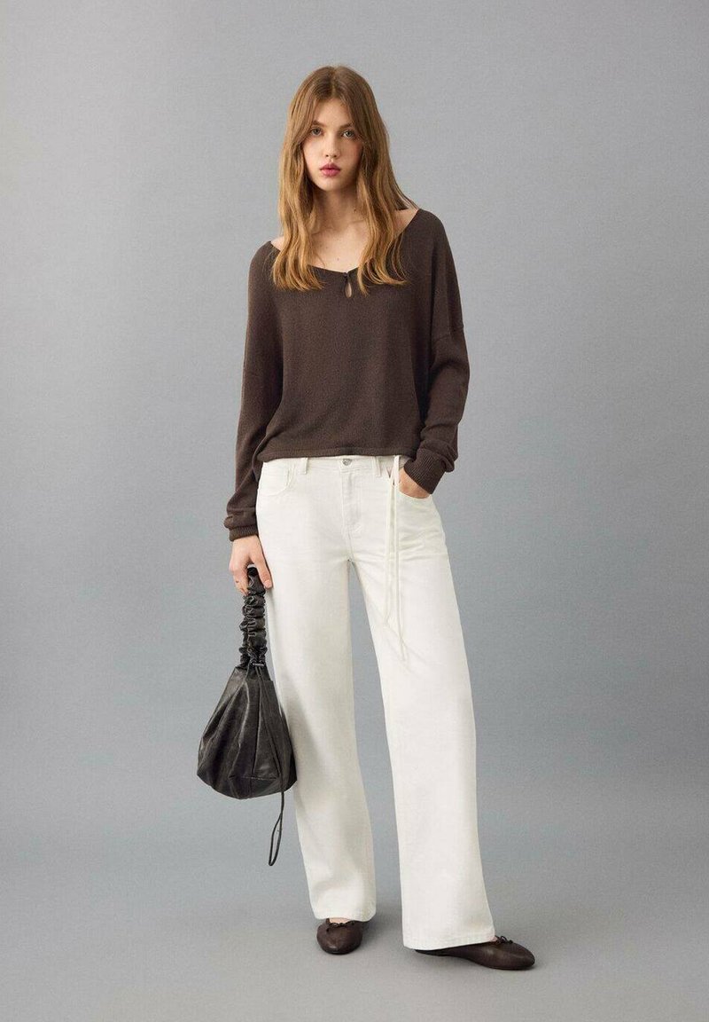 Bruin top met lange mouwen en een ronde hals, witte wijde pantalon, zwarte tas met trekkoord en donkerbruine platte schoenen. Zachte texturen en neutrale kleuren.