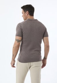 Korte ærmer, ribstrikket sweater i taupe med kabelmønster; har en smal krave og en afslappet pasform. Bæres med lyse bukser.