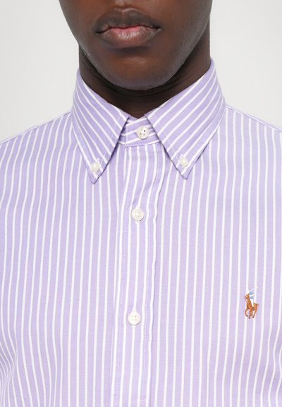 Violetinės dryžuotos marškinėliai su sagomis, su klasikine apykakle ir perlamutinėmis sagutėmis, ant krūtinės mažas žirgo raitelio emblema.