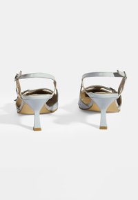 Silberne Lackleder-High-Heelsandalen mit einem schmalen Knöchelriemen, einer spitzen Zehenpartie und einem skulpturalen weißen Absatz. Glatte Textur und minimalistische Details.