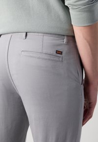 Jasnoszare spodnie z gładkiego materiału, z tylną kieszenią wykończoną cienkim szwem oraz małą czarno-pomarańczową metką "BOSS".
