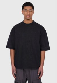 Černé oversized tričko vyrobené z bavlny, s kulatým výstřihem, krátkými rukávy a jemným logem na hrudi.