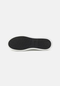 Semelle en caoutchouc noir avec motif texturé ; semelle intermédiaire blanche. Marquage visible sur la semelle. Design à bords lisses, style de baskets décontractées.