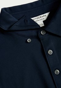 Dunkelblaues Polohemd aus Supima-Baumwolle, mit klassischem Kragen, drei Knöpfen und einer glatten, weichen Textur.