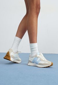 Scarpe sportive azzurre e beige con una parte superiore testurizzata, lacci bianchi e una suola in gomma marrone, abbinate a calzini bianchi a coste.