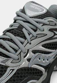 Černobílé běžecké boty s síťovaným materiálem, výrazným šněrováním, reflexními akcenty a texturovanou gumovou podrážkou.