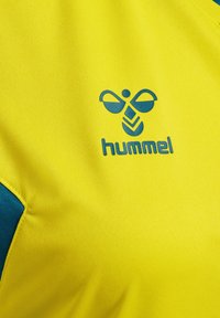 Gult sportsstof med mørkeblåt hummel-logo med stiliseret bi og brandnavn på brystområdet.